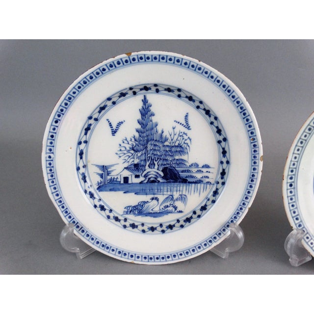 A pair of 18th-Century English Delft plates. They are hand painted in cobalt blue and white with a chinoiserie landscape...