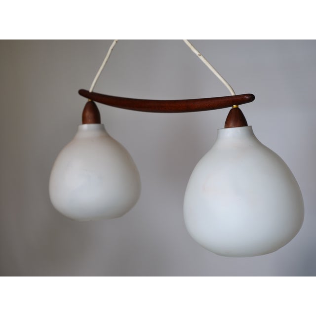 Vintage design ceiling lamp by Uno & Östen Kristiansson from the 1960s. Features two opal glass shades and a teak wood...