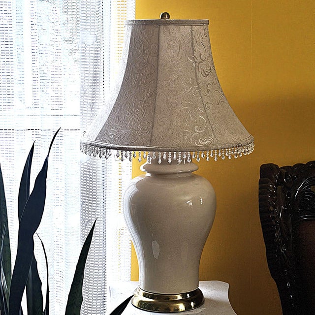 This elegant vintage table lamp features a classic ivory or rich cream glazed ceramic body with a refined baluster...