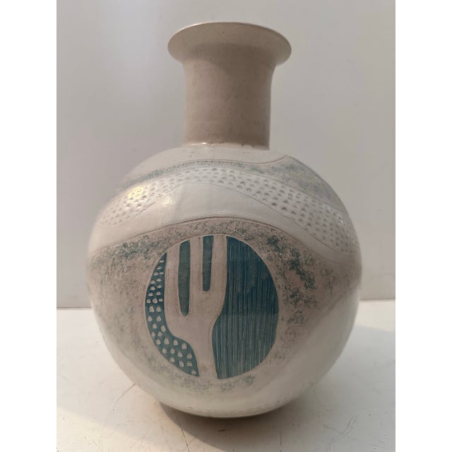 A striking handcrafted ceramic vessel featuring a rounded body and flared neck, adorned with textured relief patterns and...