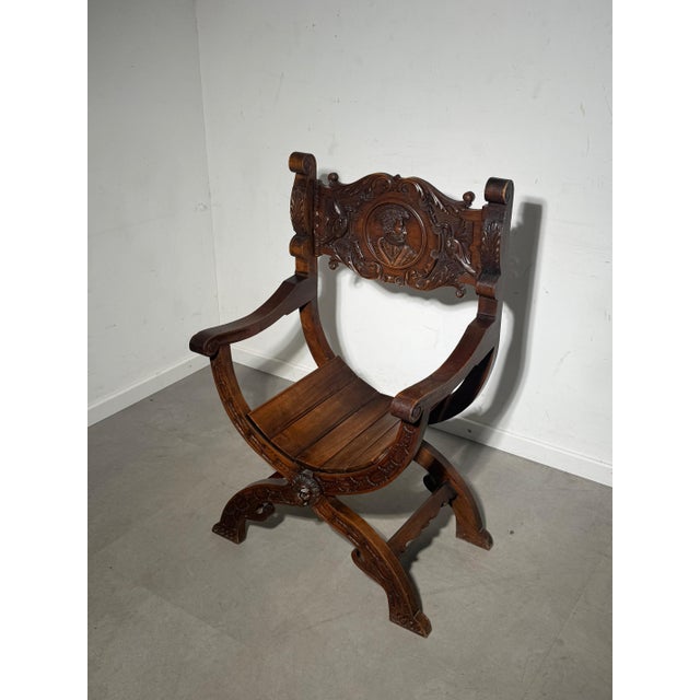 Beautiful antique Savonarola-style chair in solid oak, richly decorated with detailed hand carvings. This piece features...