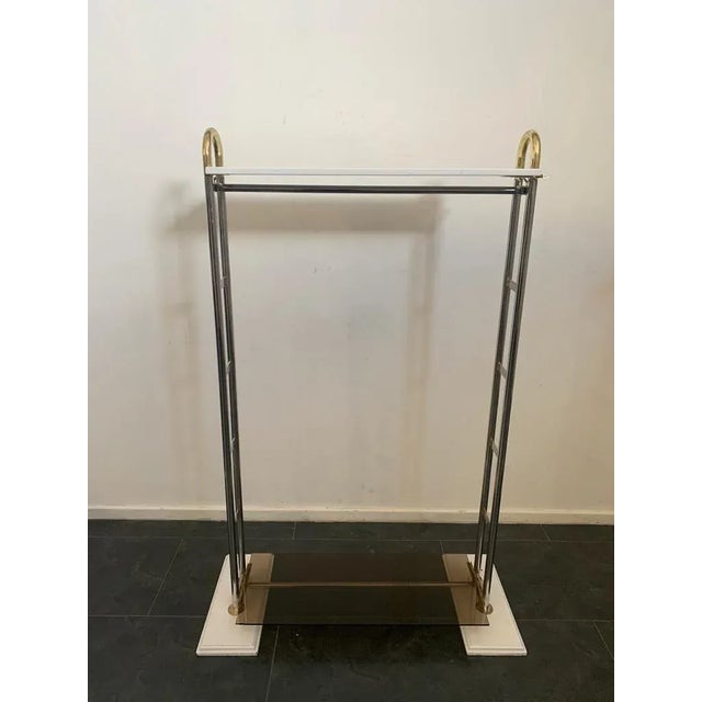 Stand steel and brass coat hanger, holds a top shelf in white lacquered wood, one lower in burnished glass, on the sides...