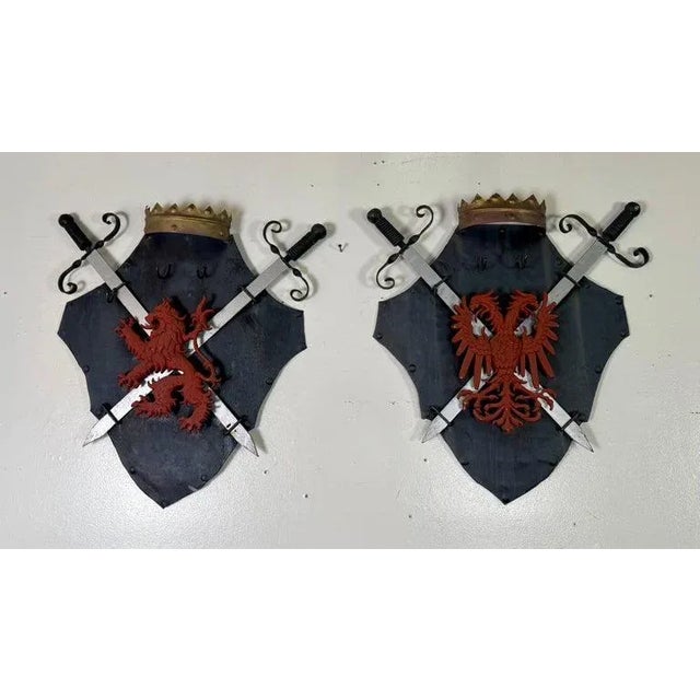 Striking pair of vintage heraldic wall plaques, each featuring a blackened shield adorned with a bold, red relief...