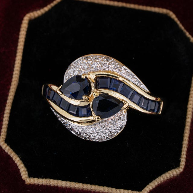 Vintage sapphire and diamond ring featuring dark blue natural sapphires accented by round brilliant cut natural diamonds...