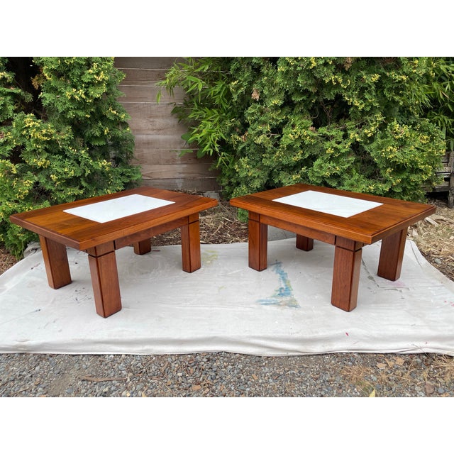 A pair of solid walnut side tables with inset marble tops. These mid-century tables feature detailed craftsmanship and...