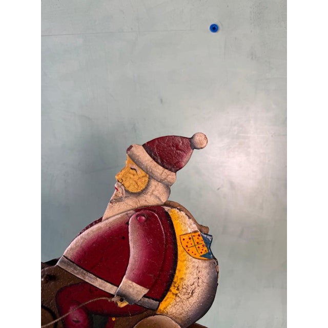 A charming vintage folk art kinetic sculpture depicting Santa Claus riding a leaping reindeer, captured in a dynamic and...