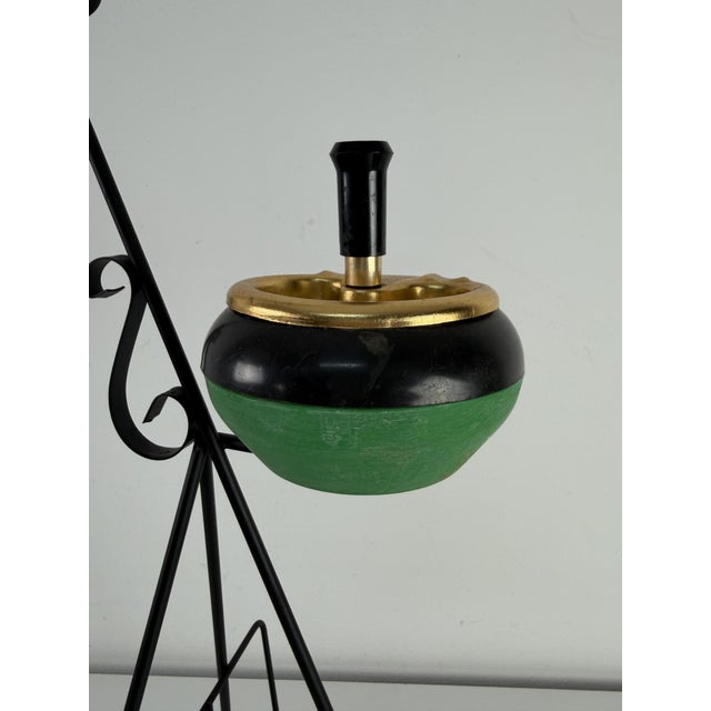 Floor-standing ashtray with magazine rack in enameled wrought iron, 1950s The ashtray features a green and gold finish....
