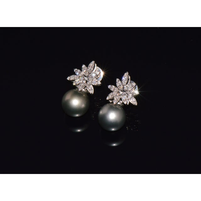 These earrings feature an elegant starburst diamond cluster design centered around perfectly matched natural Tahitian...
