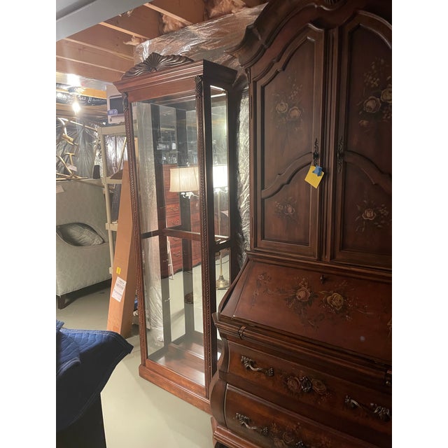 It’s a very traditional curio display cabinet carved leaves and pineapples. Dark wood. Glass shelves. Mirrored back and In...