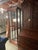 It’s a very traditional curio display cabinet carved leaves and pineapples. Dark wood. Glass shelves. Mirrored back and In...