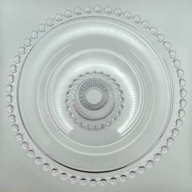 A small round pressed glass dessert stand with a beaded rim & foot on a solid clear background in the Candlewick pattern.