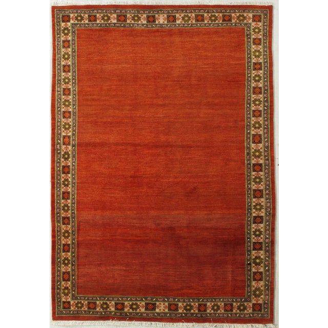 Vintage hand-knotted Persian Gabbeh rug featuring a rich red field framed by a decorative border with stylized floral and...