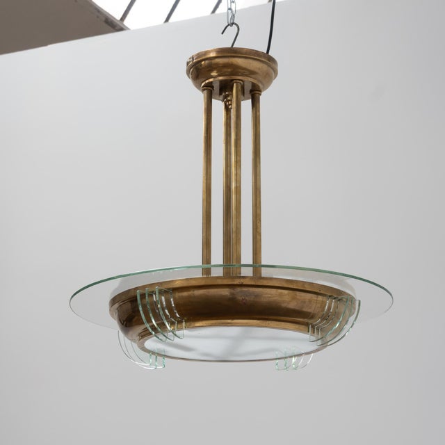 An elegant Art Deco chandelier, crafted from brass and glass, with architectural lines and a sculptural presence. The...
