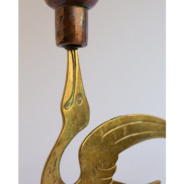A pair of Scandinavian brass candleholders, each shaped as a stylised bird with an elongated neck supporting a copper...