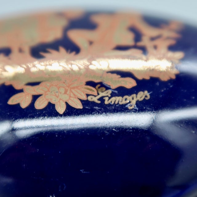 A charming cobalt blue Limoges porcelain trinket box featuring a gilt courting scene — a seated woman with fan and a...