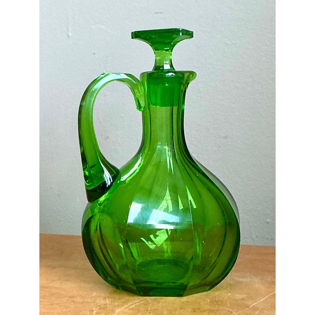 This vintage glass decanter presents a vibrant green hue with a smooth, glossy finish, its bulbous body gracefully...