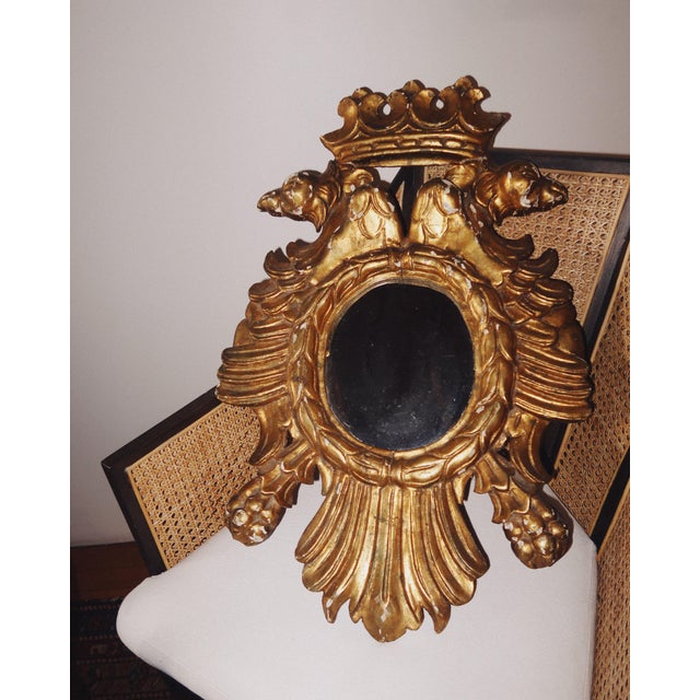 A richly carved antique European giltwood wall mirror featuring a crowned double eagle crest above an oval mirror plate....