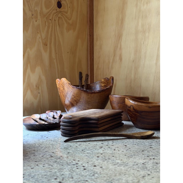 A curated collection of hand-carved olive wood serveware, each piece shaped from a single block of wood and finished to...