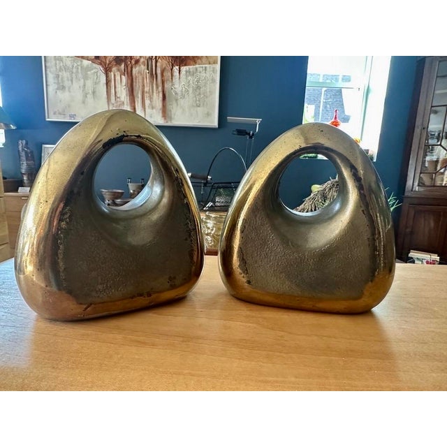 Ben Seibel Orb bookends in brass. Pair of rounded sculptural brass over white metal bookends with cutout handles. The warm...