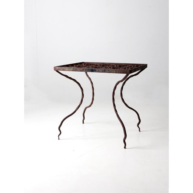 This early 20th-century wrought iron table features a grid-like tabletop with swirling, flower-inspired shapes. Twisted...