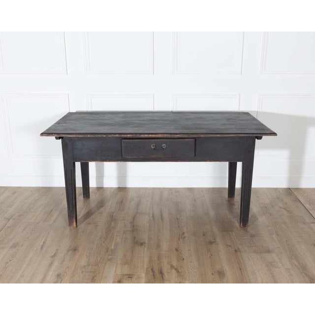 A handsome Swedish country kitchen table crafted from solid pine and finished in a worn, matte black paint that highlights...