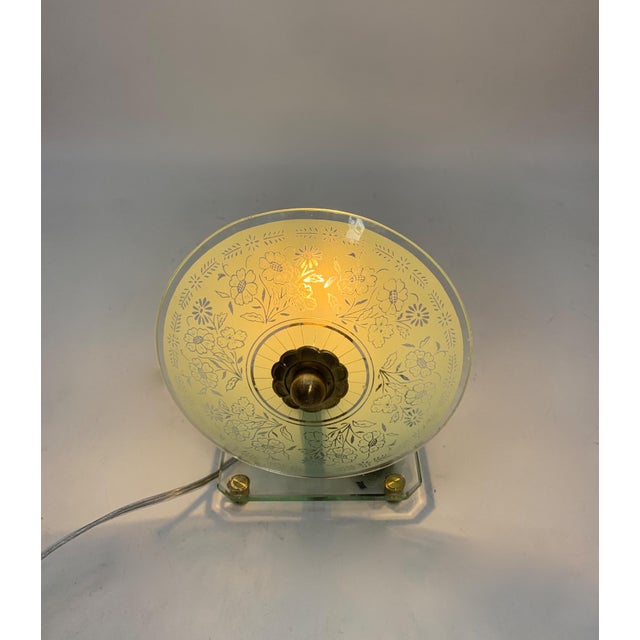 Decorative clear glass base with a square shape and rounded corners, supported by small cylindrical gold-plated metal...
