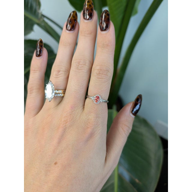 A 0.40-carat padparadscha sapphire oval sits at the centre of this solid 14K white gold ring, framed by eighteen earth-...