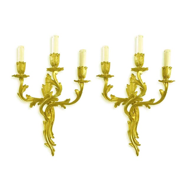 A pair of Louis XV-style gilded bronze sconces, featuring vegetal and shaped branches with three arms terminating in beige...