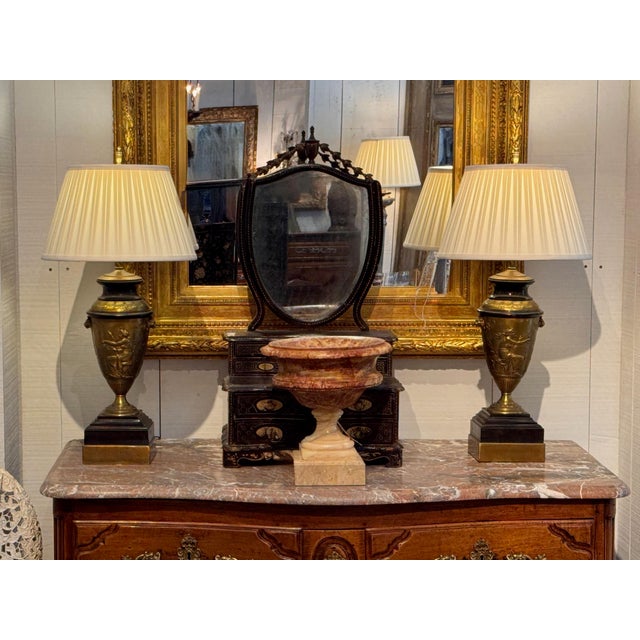 A pair of gilded bronze urn-form lamps with neoclassical relief figures and lion mask handles, mounted on stepped marble...