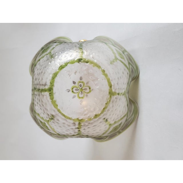 Gilded art glass basket with scalloped rim and ornate gold-tone handle. Translucent green and white textured glass is...