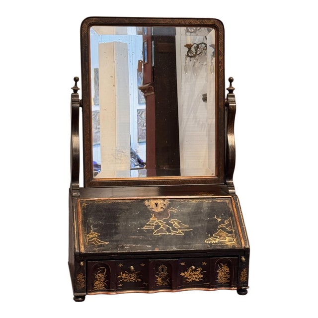A dressing mirror with a rectangular tilting glass set in a dark frame above a slant-front compartment decorated with...
