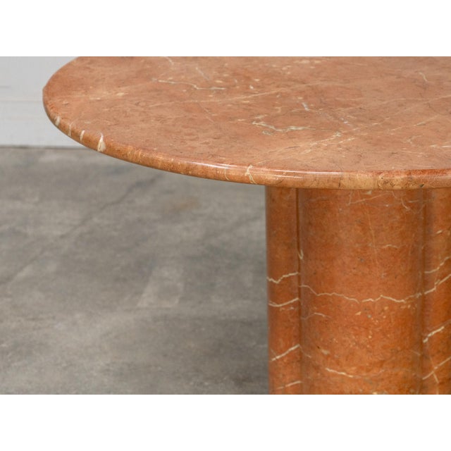 A round red travertine table attributed to Mario Bellini, dating from the 1970s. Its circular top with rounded edges rests...
