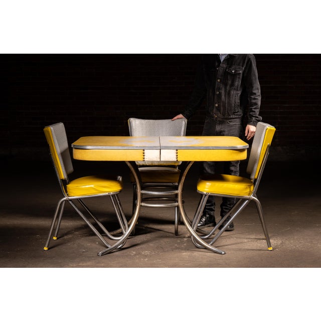 Mid-century "Plasticove" dinette set featuring a drop-leaf laminate table and three matching vinyl chairs. The tabletop is...