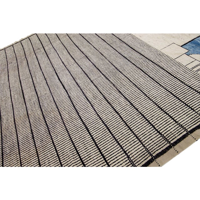 Beautiful Moroccan-style hand-knotted wool rug with a beige field. This oversize rug has black and blue accents in an all-...