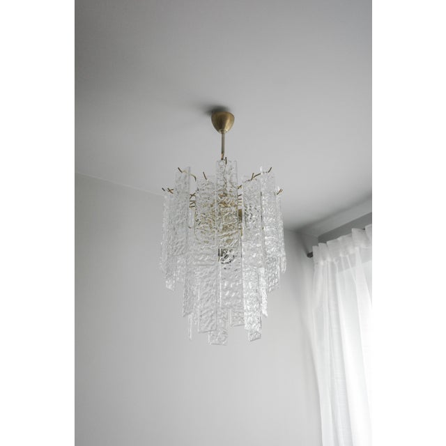 The chandelier is made of a cascade of clear Murano glass petals, suspended from a metal frame and chain, which give it...