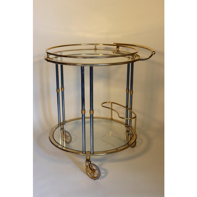 of circular form with two glass tiers, the top with a handle, the bottom with a bottle holder, on three wheels