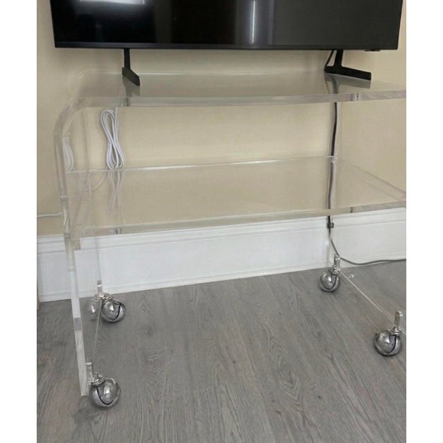 Custom-fabricated clear acrylic waterfall media console on smooth-rolling chrome casters. Engineered from premium, ultra-...