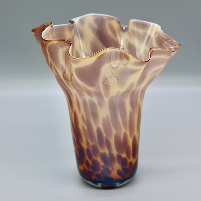 A hand-blown handkerchief vase in a tortoiseshell pattern that shifts with the light — creamy opaque glass mottled in...