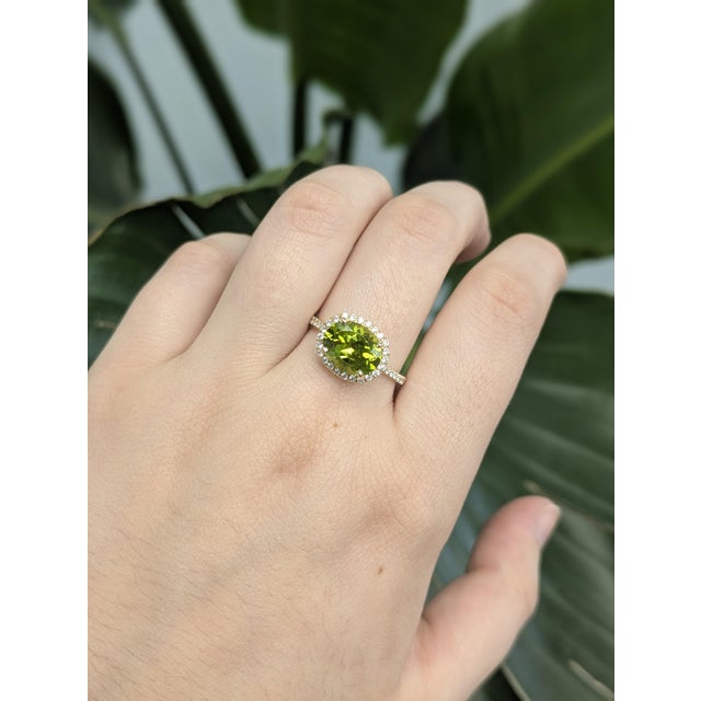 Set in solid gold and accented with sparkling diamonds, this stunning ring features a vivid 2.93ct oval-cut Peridot...