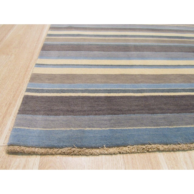 A 5' 6" x 8' hand-knotted wool rug with narrow stripes of slate blue, mocha, ivory and silver. Newly made in India. Size:...