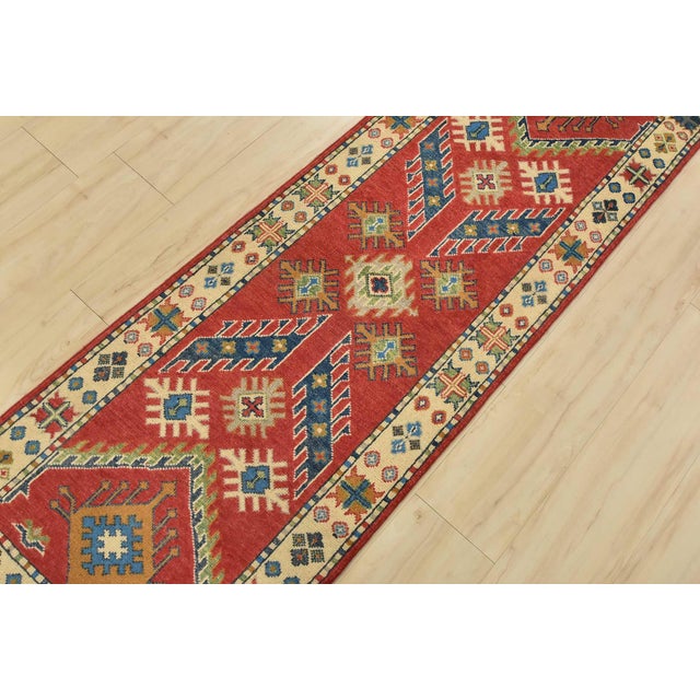 A tribal Caucasian Kazak runner hand-knotted with fine wool on a cotton foundation. This rug features geometric motifs set...