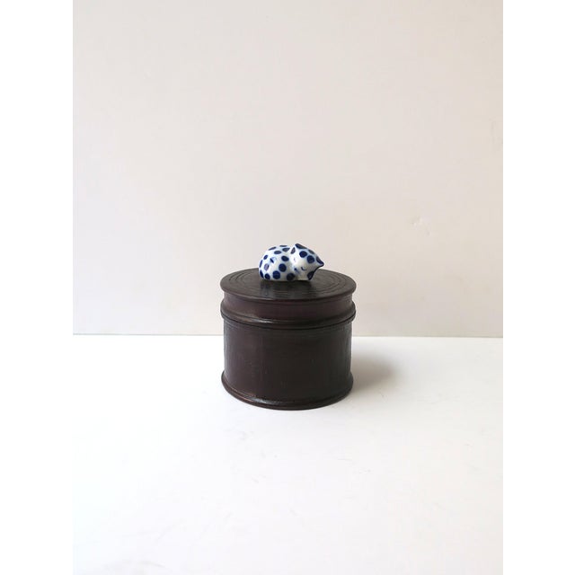 A rich dark brown teak trinket or jewelry box with a blue‑and‑white porcelain cat finial, circa mid‑20th century. A round...