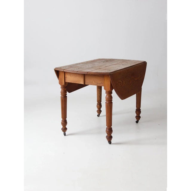 This is an antique wood table with drop leaf extensions. The wooden table features turned legs with casters. The...