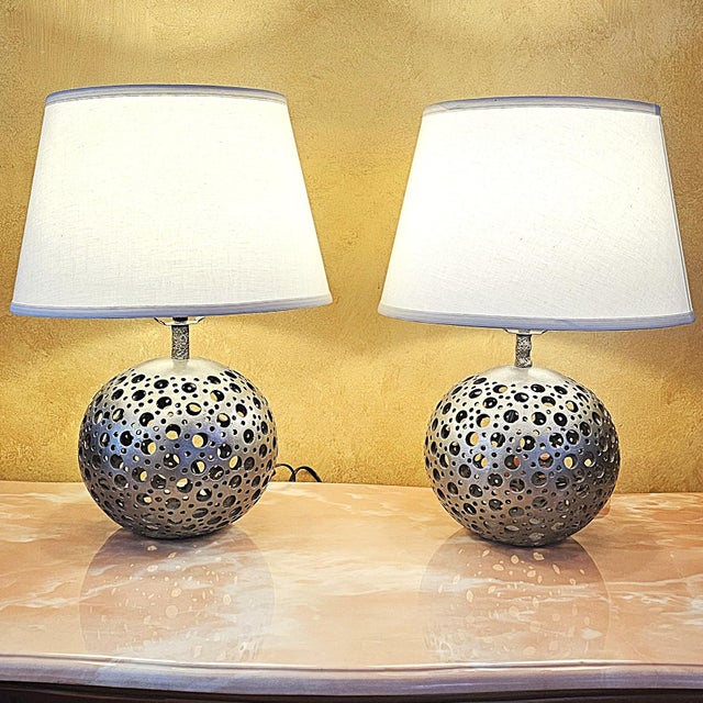 A refined pair of sculptural table lamps crafted from pierced pewter, featuring spherical bases with an elegant openwork...