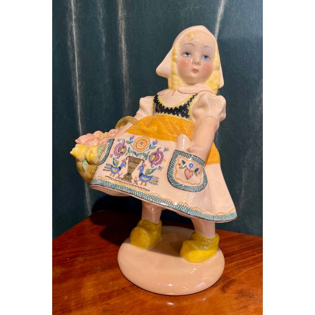 Ceramic depicting a flower girl in traditional Dutch dress with a basket of flowers by the Essevi factory. This piece has...