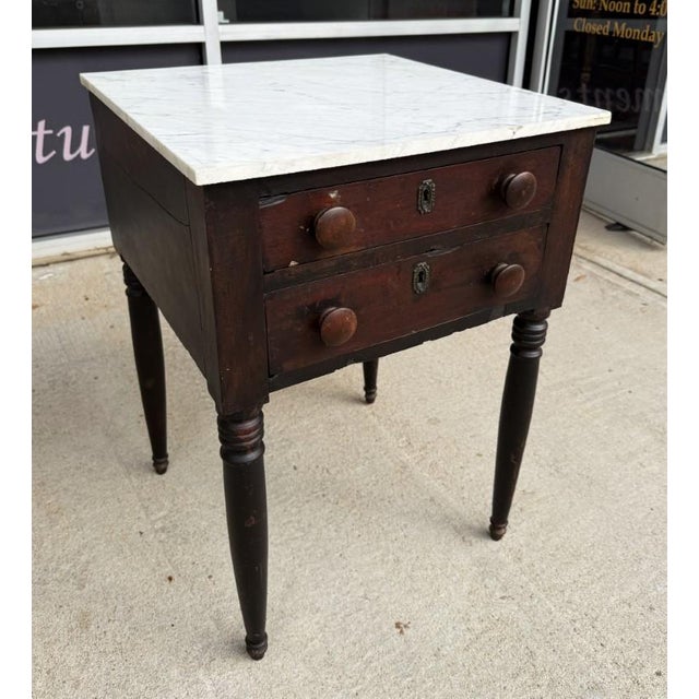 This 19th-century end table features a solid marble top set above a two-drawer wooden base, retaining its original,...