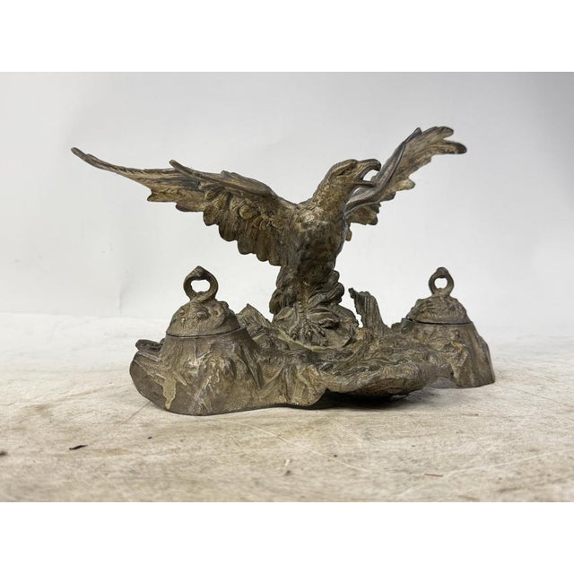 Elegant vintage inkwell featuring a sculpture of an eagle with outstretched wings. The base has two inkwells with lids. A...