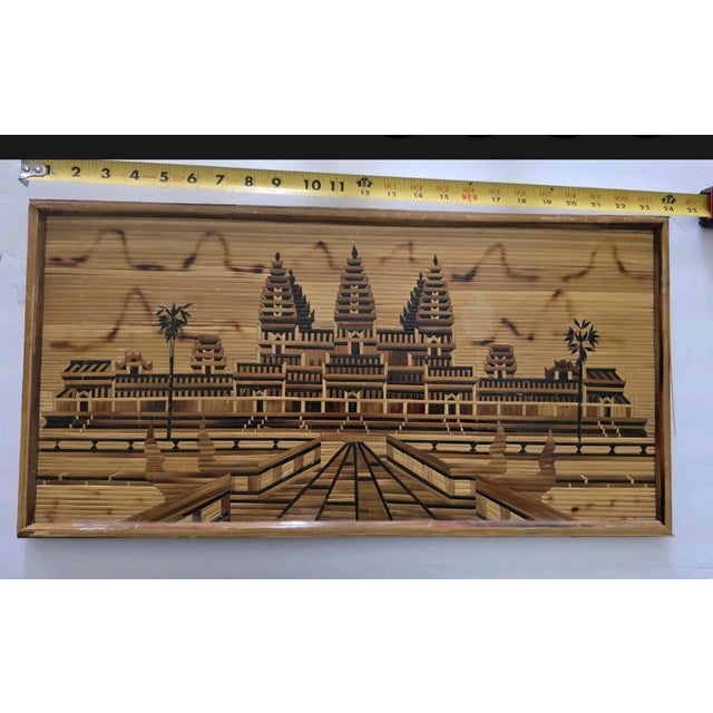 The framed art appears to be a Khmer wood mosaic or marquetry art piece depicting Angkor Wat, a renowned temple complex in...