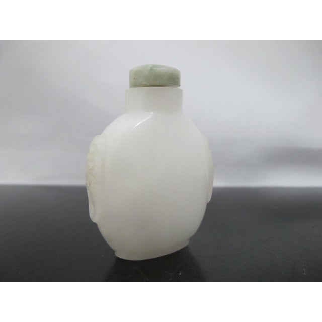 Chinese white peking glass snuff bottle with green stopper, spoon intact. Ovoid shape showing carved mask design along...