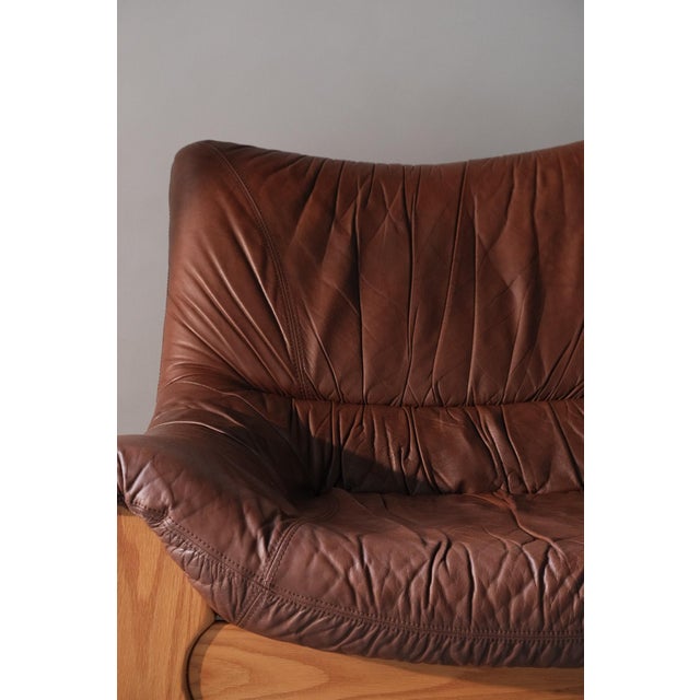 Low, wide three-seater sofa in solid elm and leather, France, 1960s-70s, by Maison Regain. It seats three to four people...